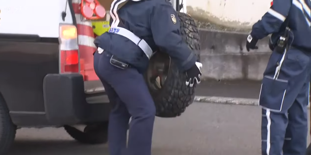 はずれた軽自動車のタイヤは警官が持ち上げるのも苦労する重さ。